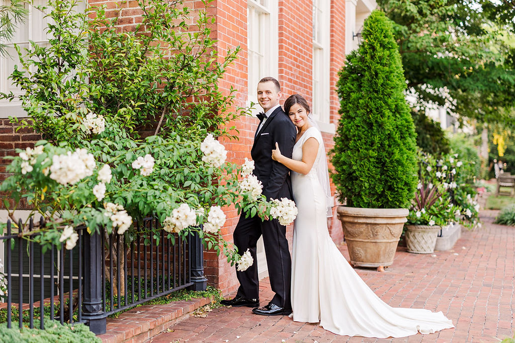 bride hugging on her groom in front of a rose bush at their old town alexandria wedding