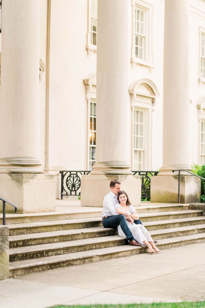 man holding his fiance while sitting on the stairs of VMFA Engagement Photos Richmond VA