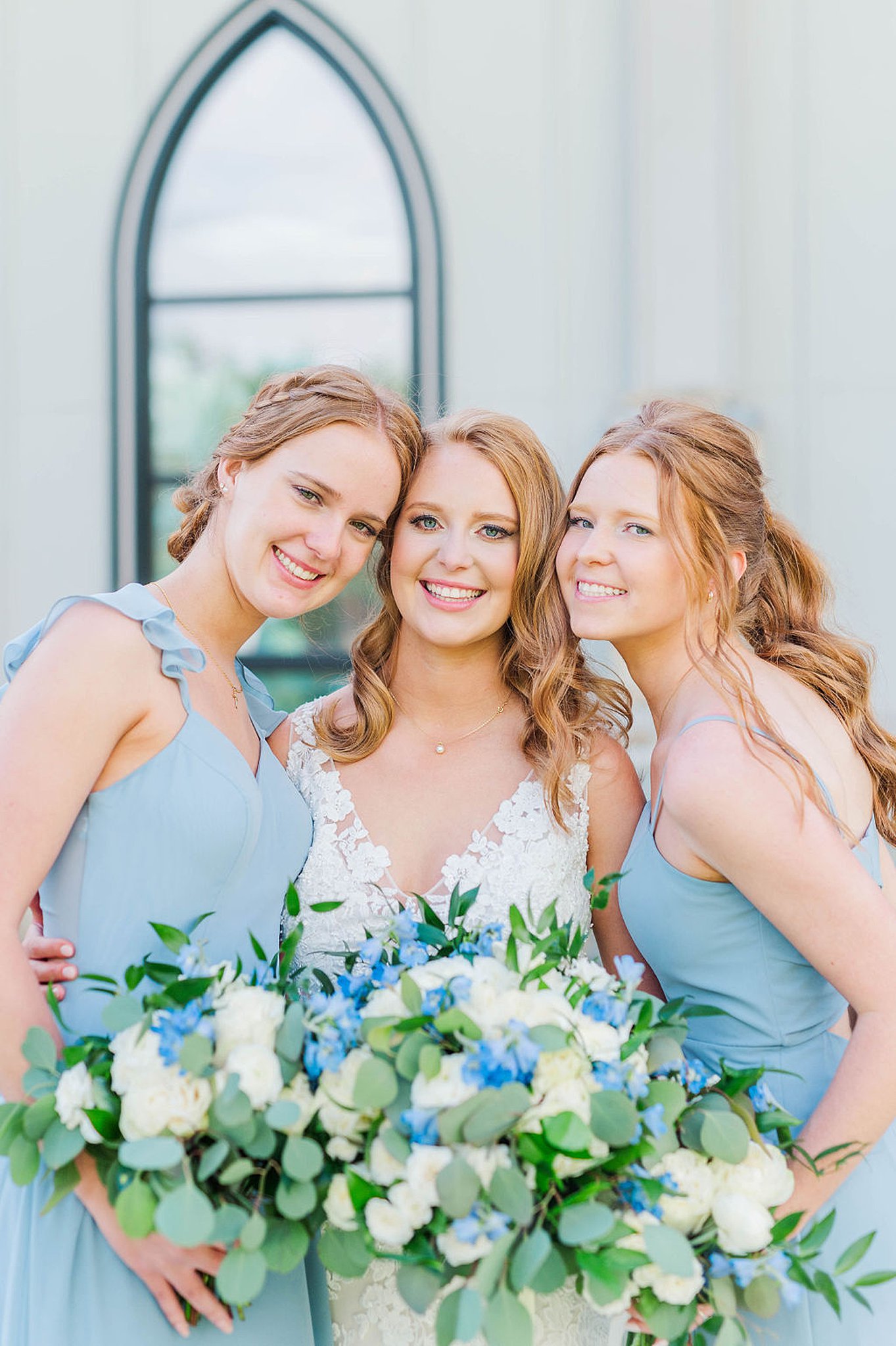 bridesmaids press heads against bride holding blue bouquets