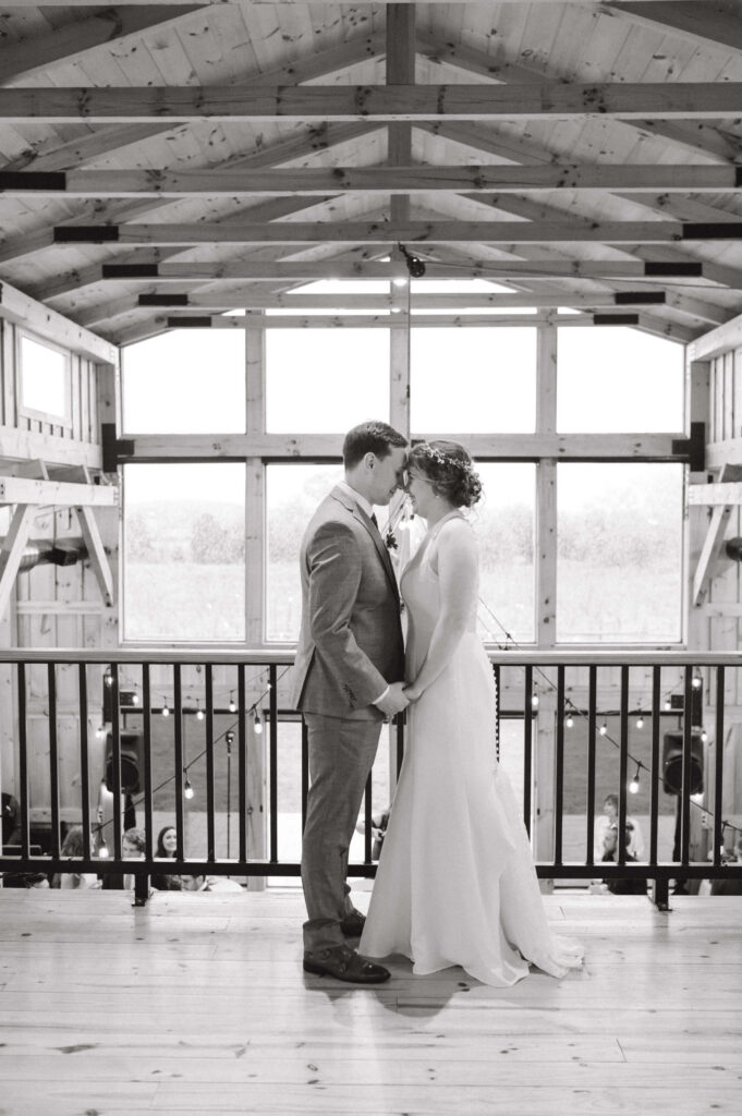 wedding couple posing inside a barn wedding venue overlooking reception