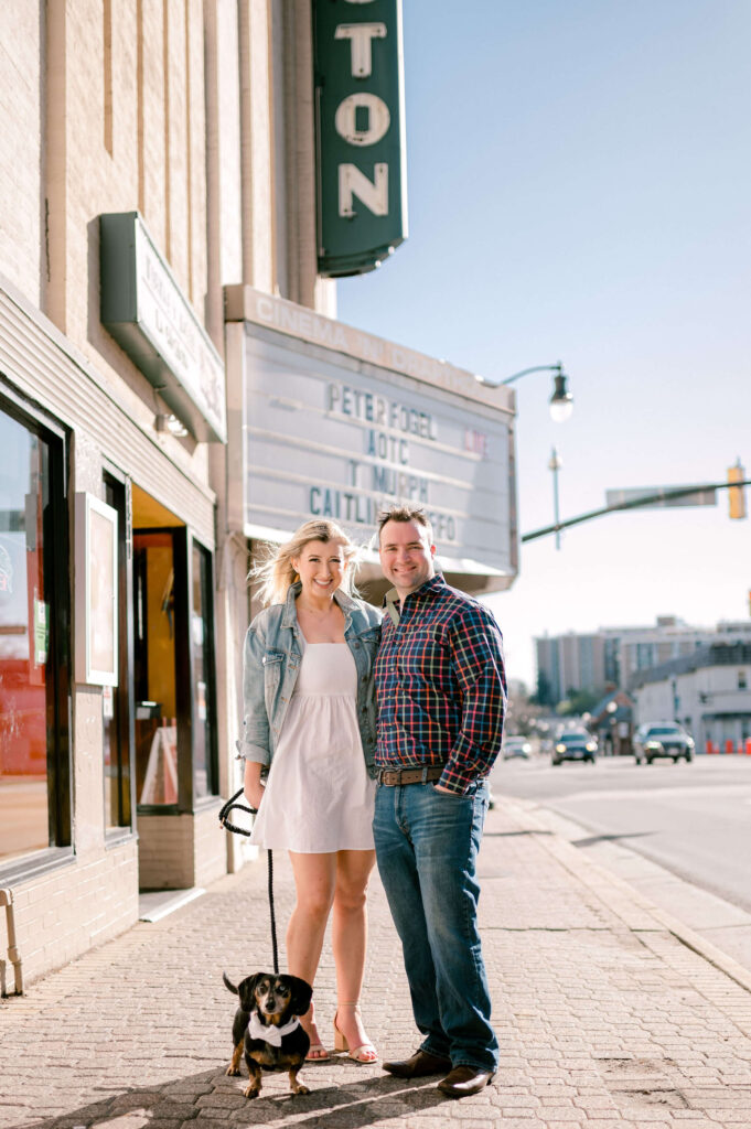 couple in front of movie theater with daschund during engagement photo with their dog