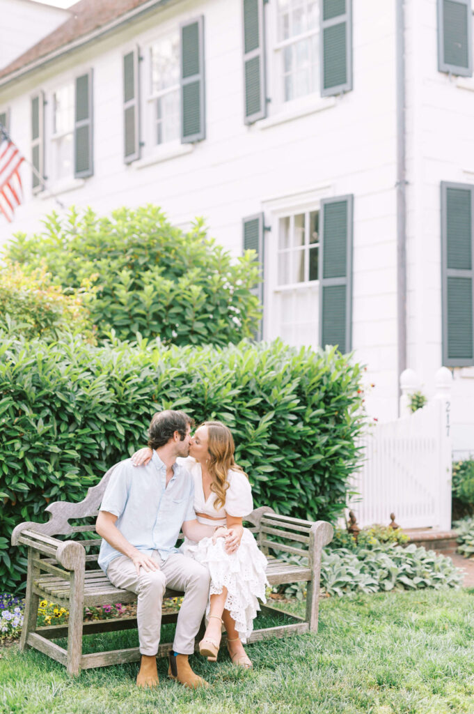 couple kissing on bench outside of a white house