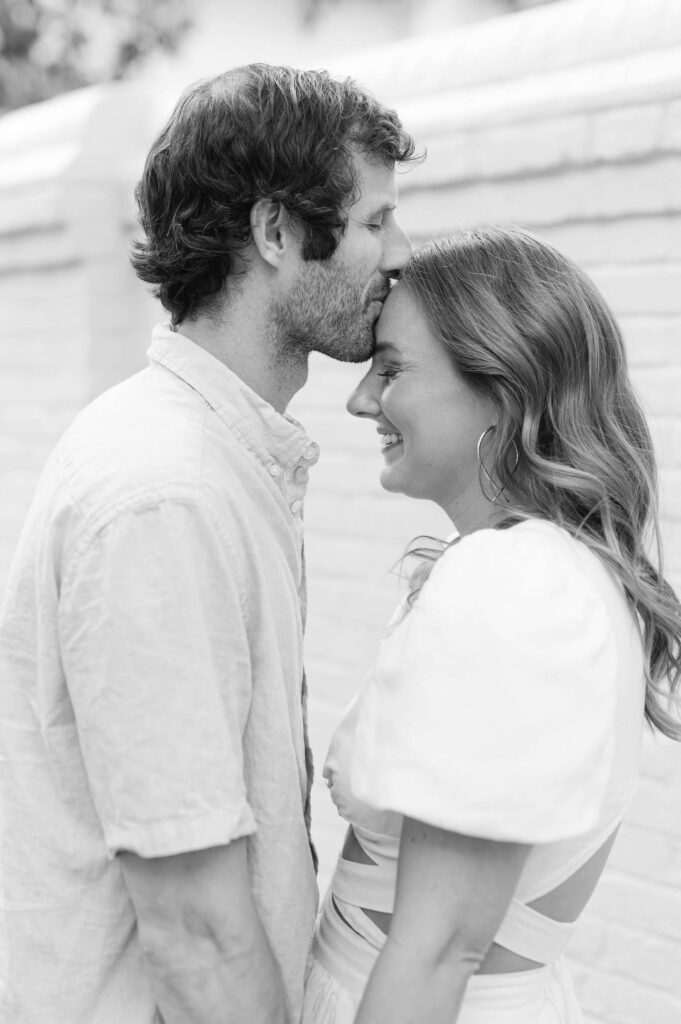 Black and white engagement photos of groom kissing bride on forhead