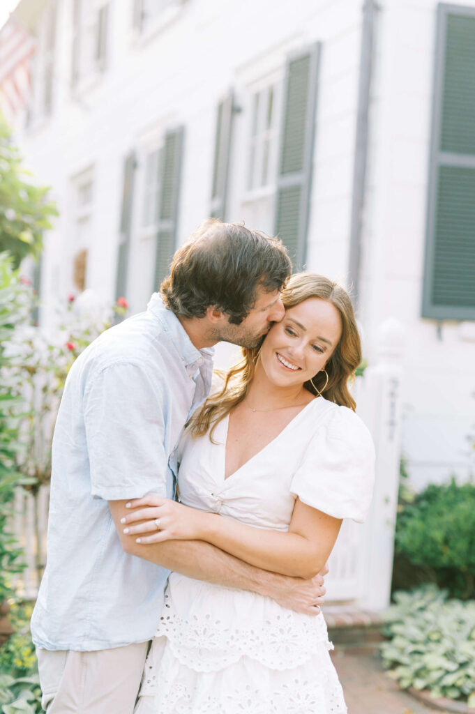 engagement photos in front of house in Old Town Alexandria with man kissing woman on cheek