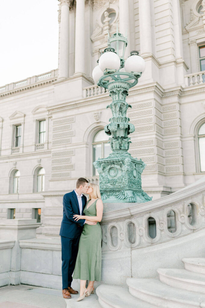 A couple kissing in front of a green lamppost outside of the Library of Congress.
