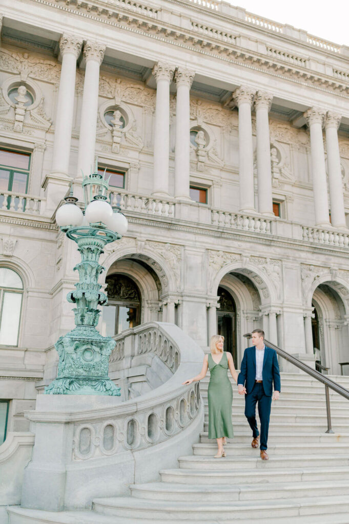 An engaged couple holding hands and walking along the staircase at the Library of Congress
