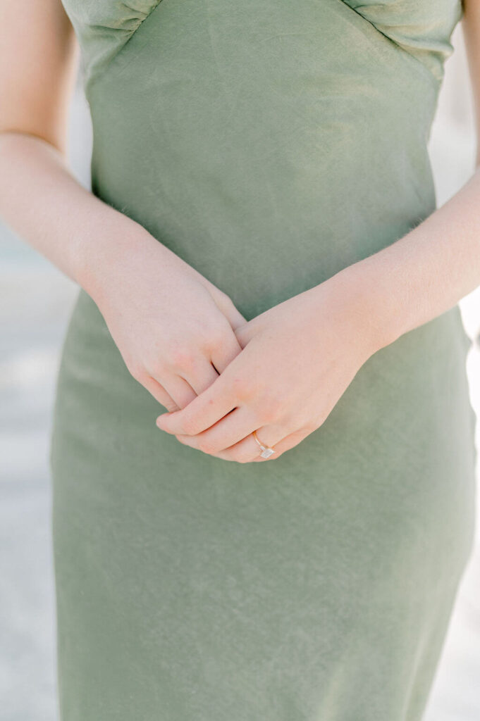 Detail image of a woman pinching her hands together against her green PepperMayo dress.
