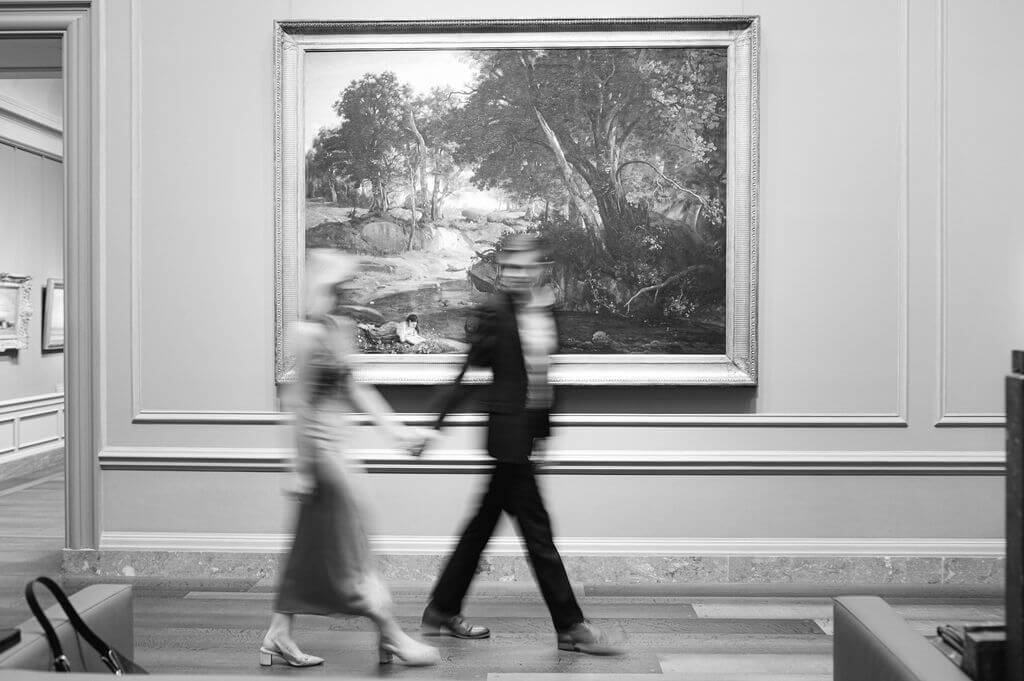 Black and white blurry image of a couple walking through an art gallery.
