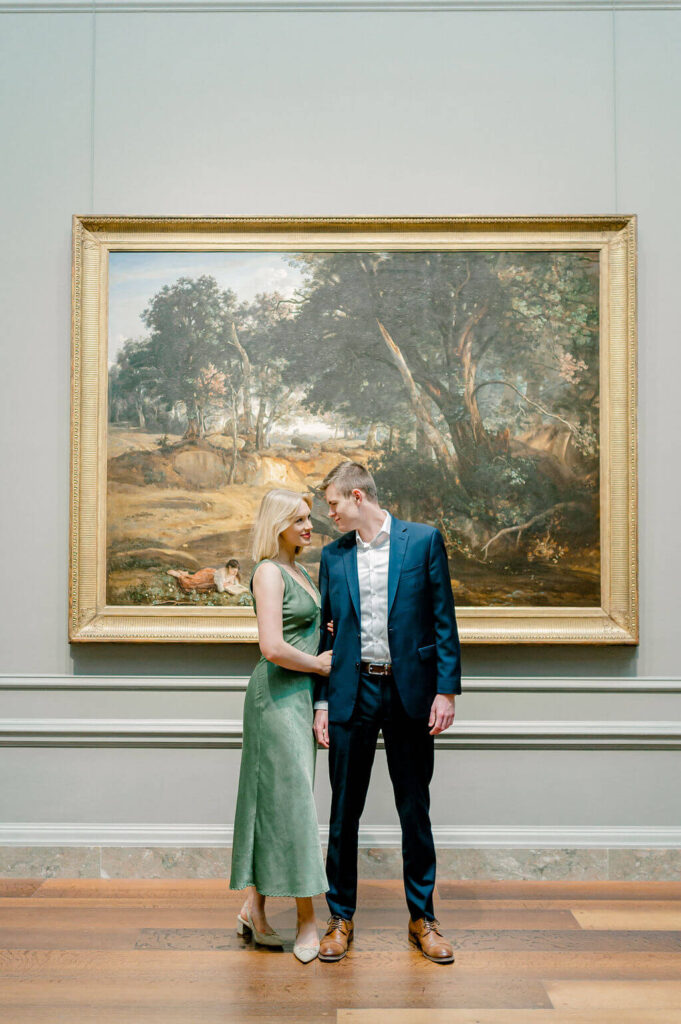 Couple looking at each other with a piece of art in the background.
