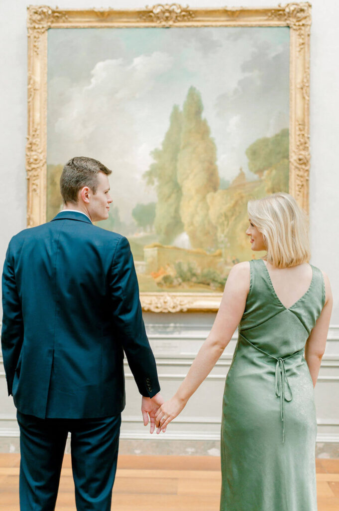 Couple holding hands while looking at a piece of art. 