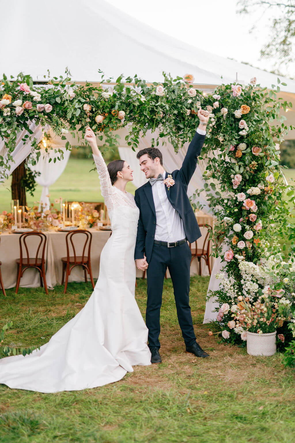 Joyful bride and groom celebrating under a floral arch in front of their tented reception at The Willows at Ashcombe Mansion.
