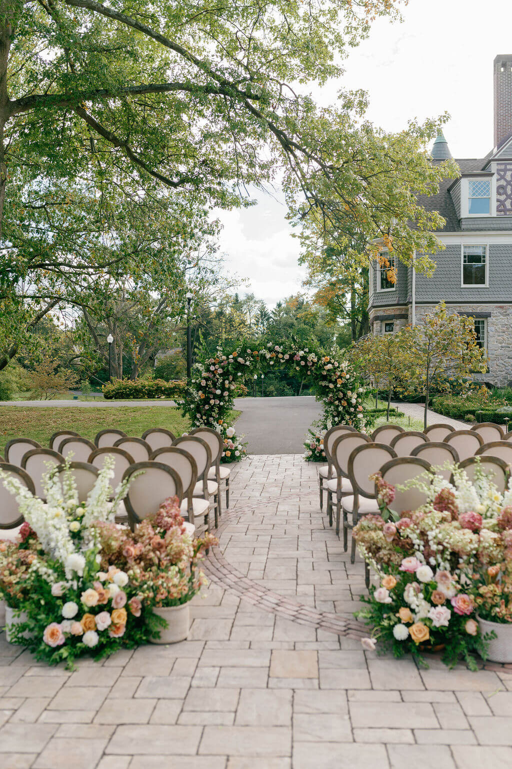 Ceremony setup at The Willows at Ashcombe Mansion featuring flower-lined aisles, vintage chairs, and a floral arch.