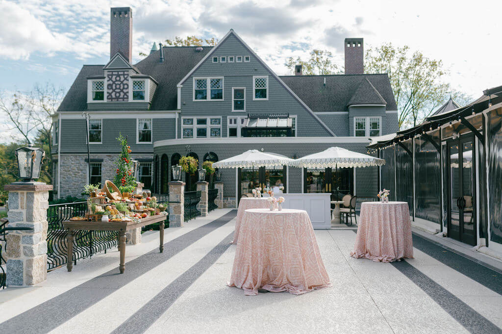 Outdoor cocktail hour setup at The Willows at Ashcombe Mansion featuring bistro tables and a grazing table.
