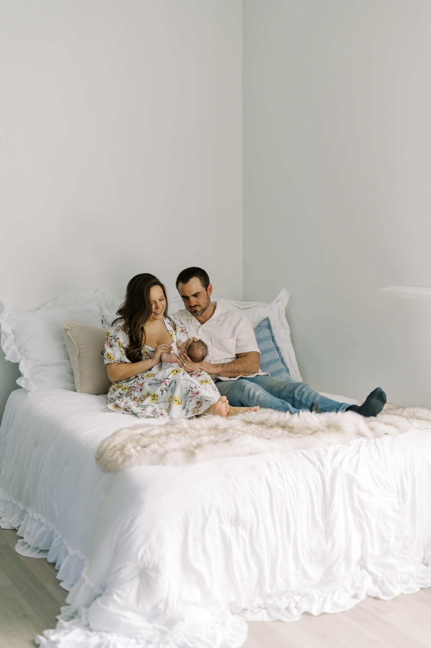 New parents snuggle on a bed playing with their newborn daughter in mom's lap