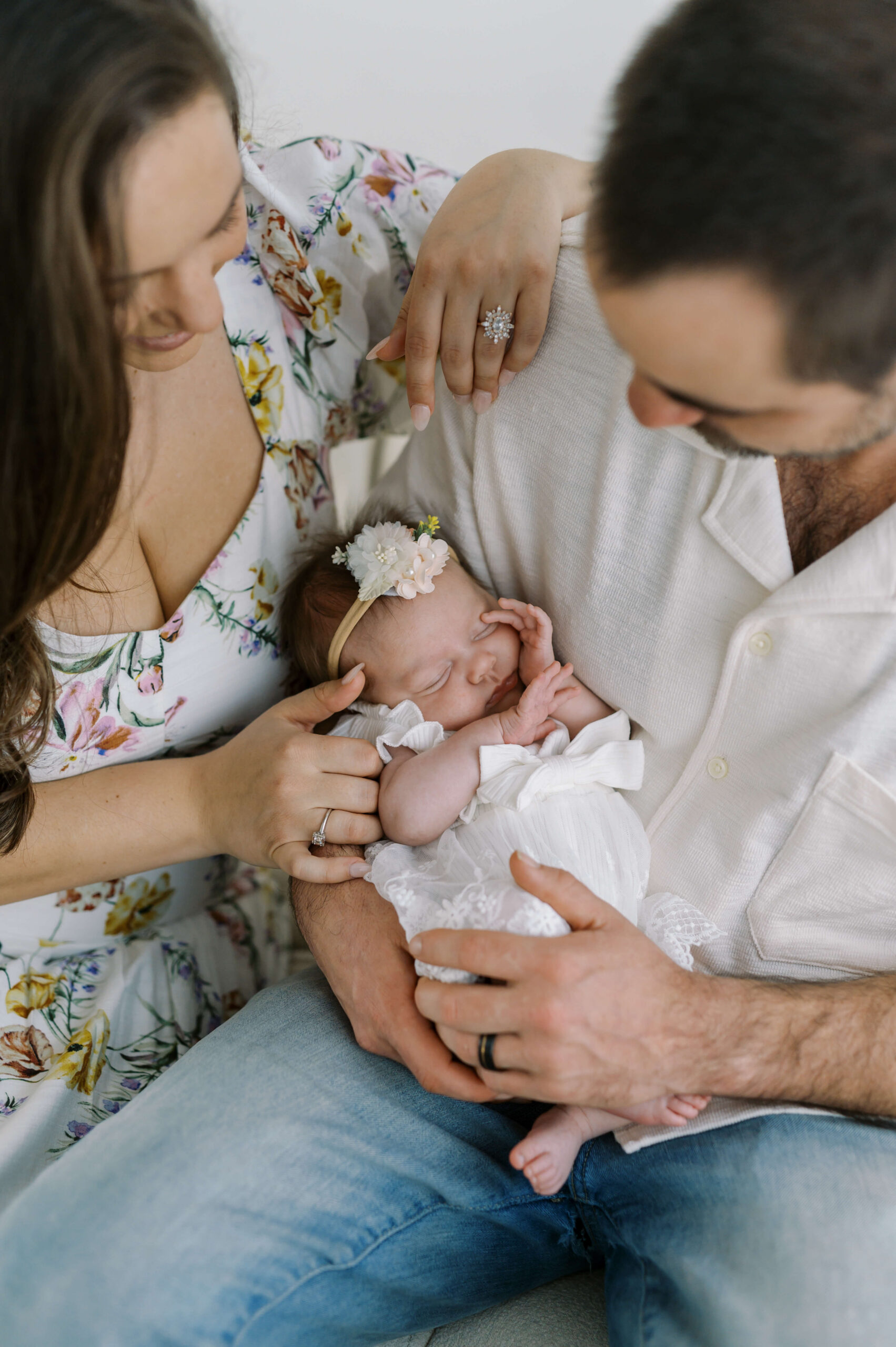 A look down at a sleeping newborn girl in a white dress in dad's lap after visiting baby boutiques in richmond va
