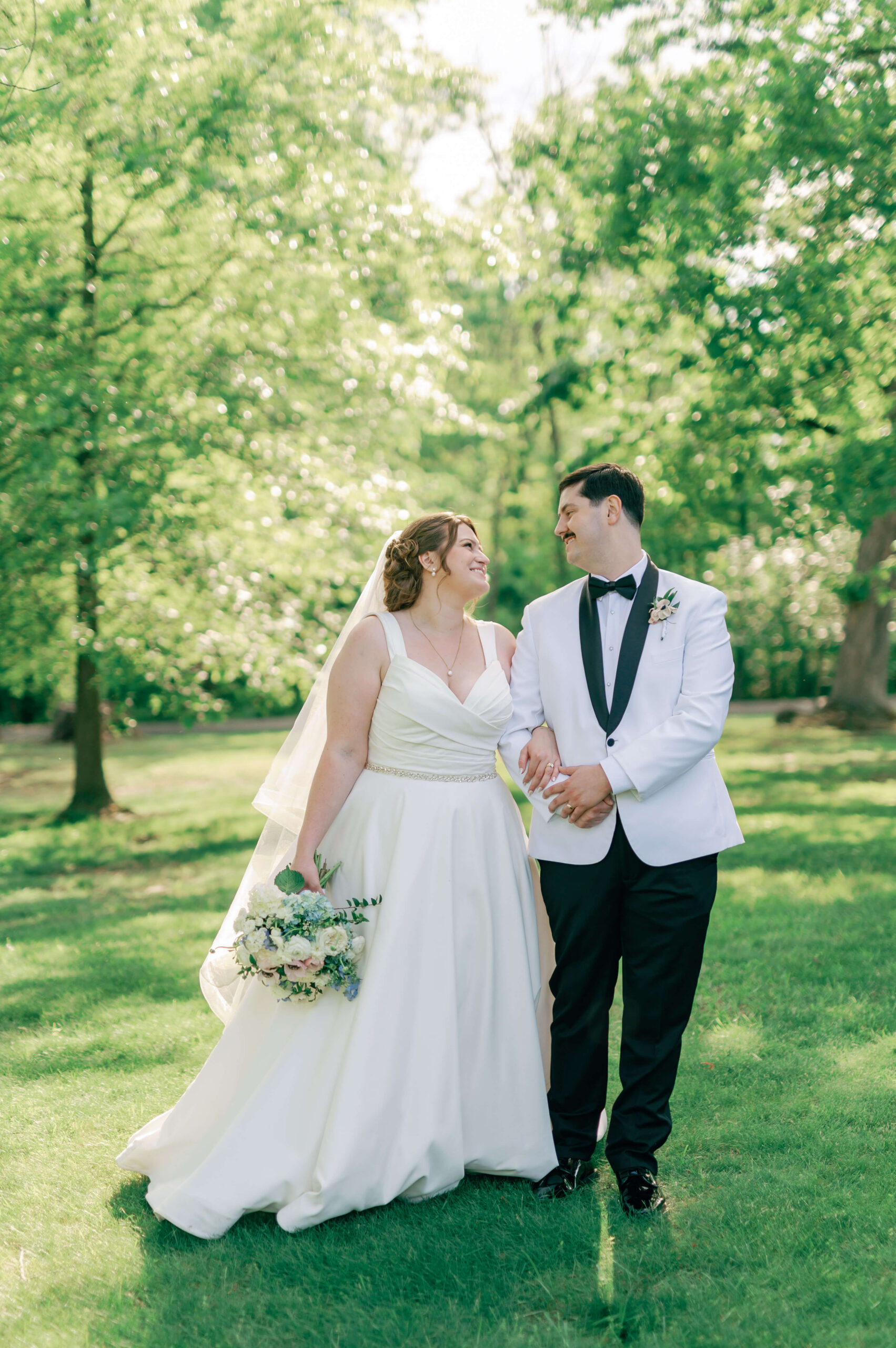 A bride and groom walk in a lawn at sunset smiling at each other during their clifton inn wedding