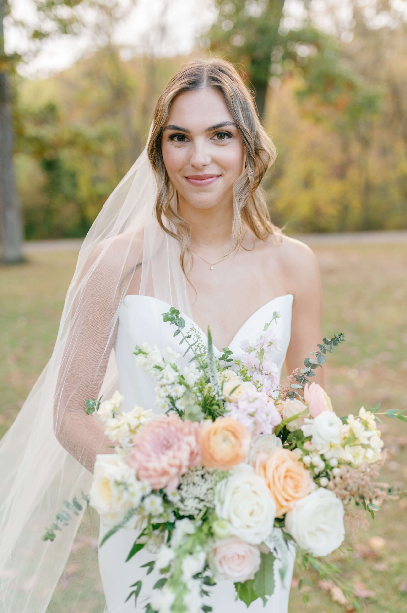 A smiling bride holding her large bouquet in. lawn at sunset during her keswick hall wedding
