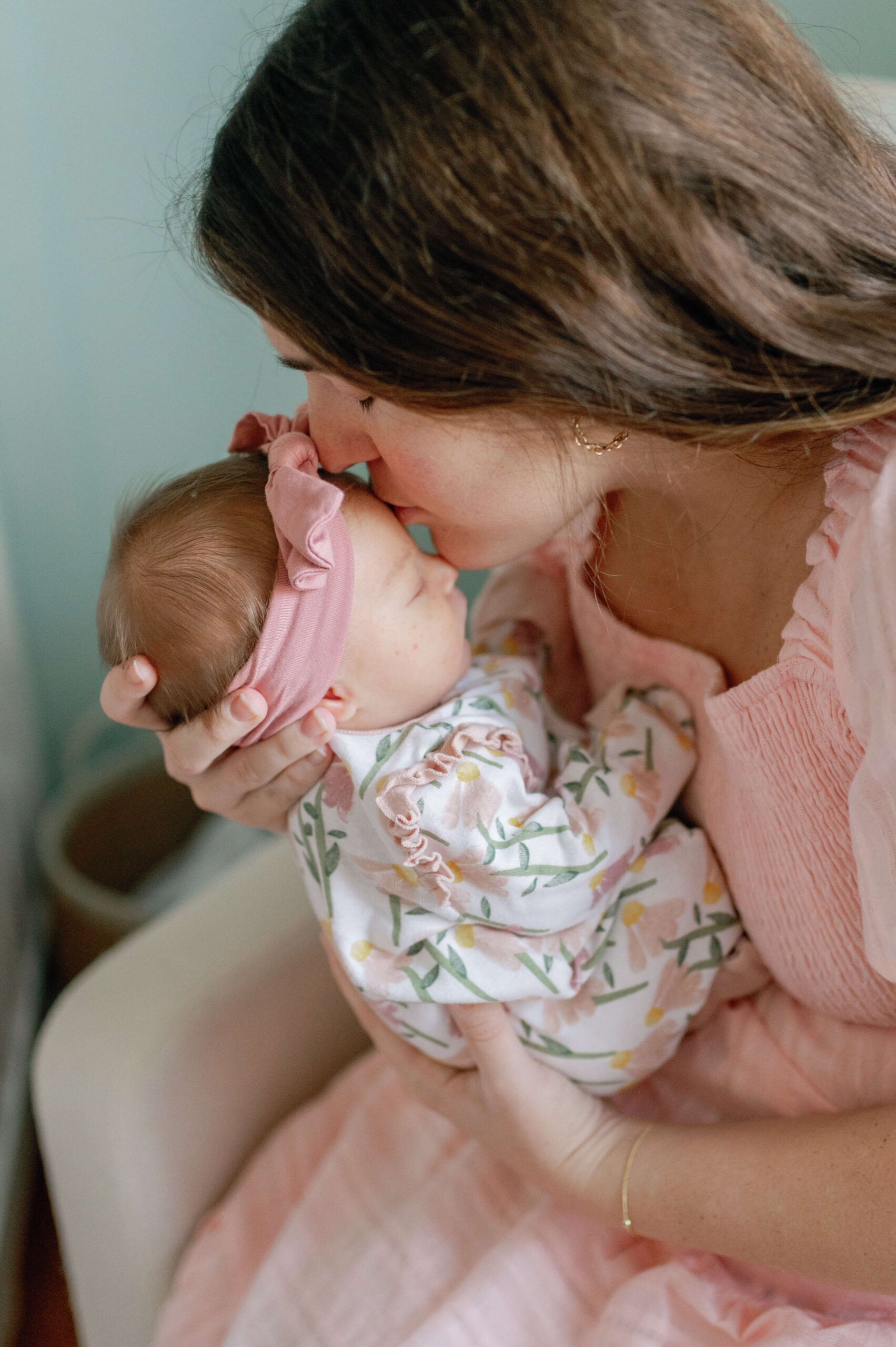 A new mom kisses the forehead of her newborn daughter while sitting in a nursing chair