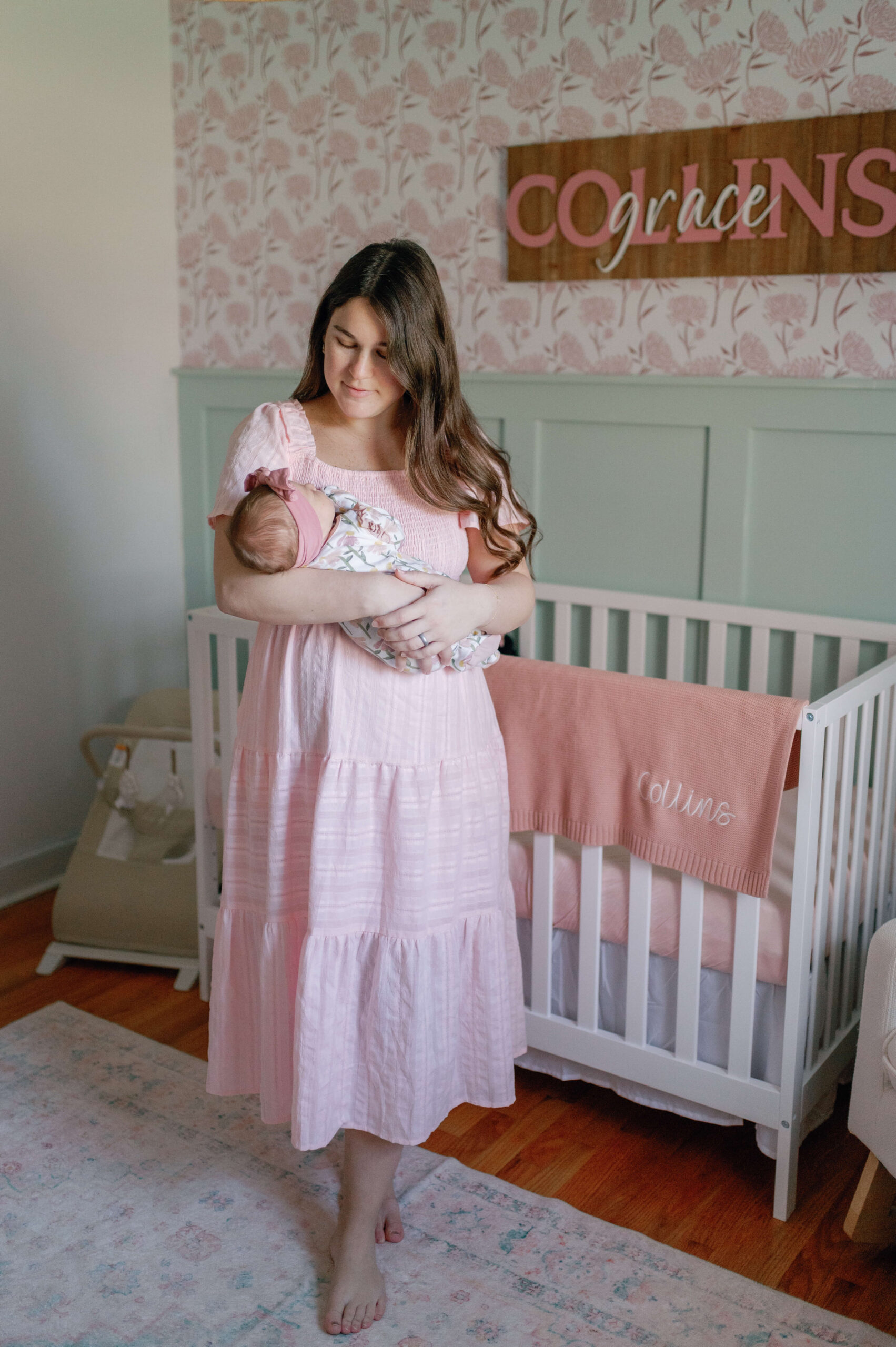 A happy new mom stands in a nursery cradling her sleeping newborn daughter in her arms thanks to lactation consultants in richmond