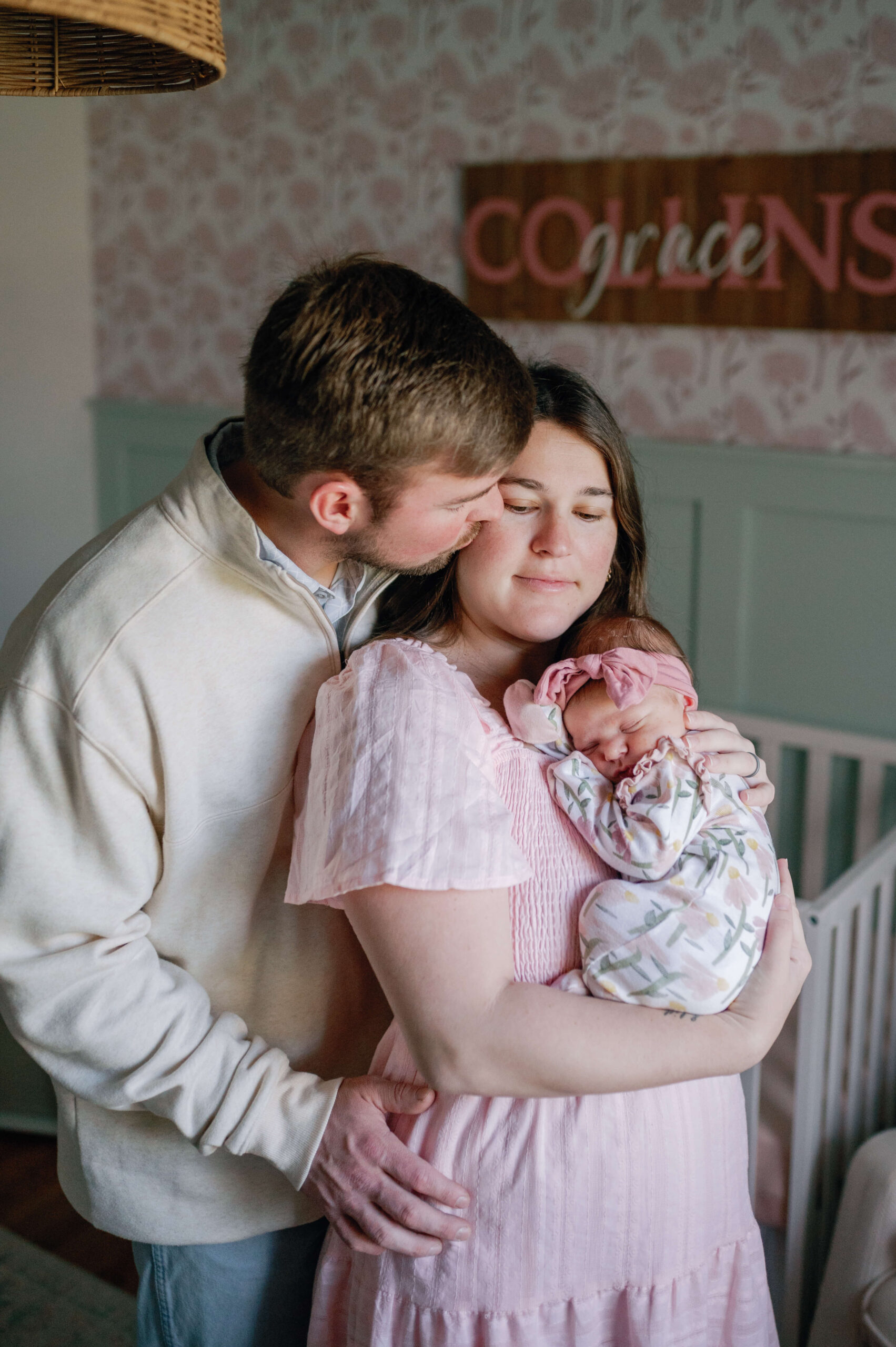 Happy mom and dad snuggle in a nursery with their sleeping newborn against mom's chest thanks to lactation consultants in richmond