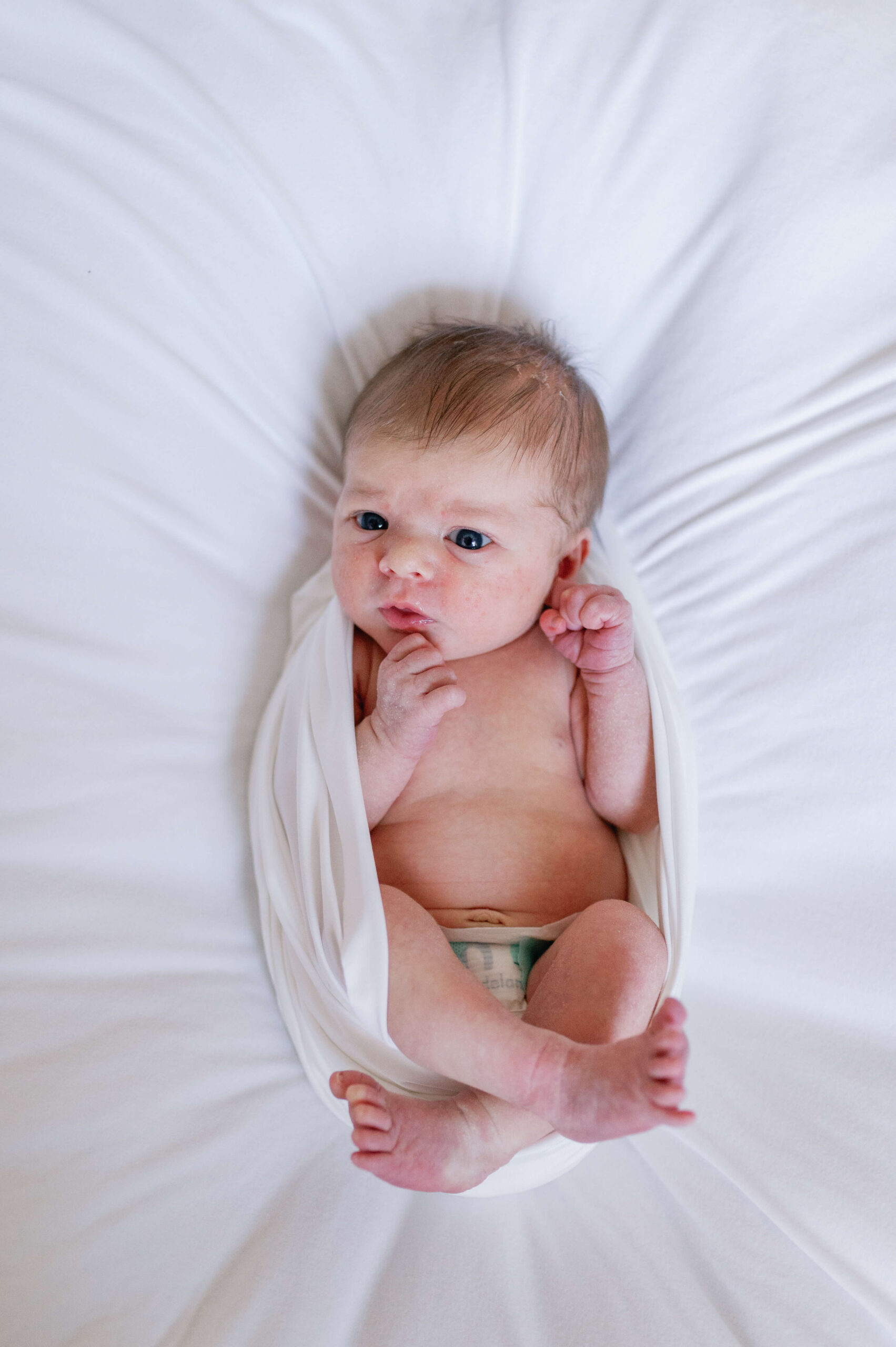 A newborn baby lays awake in a white open top swaddle after meeting lactation consultants in richmond