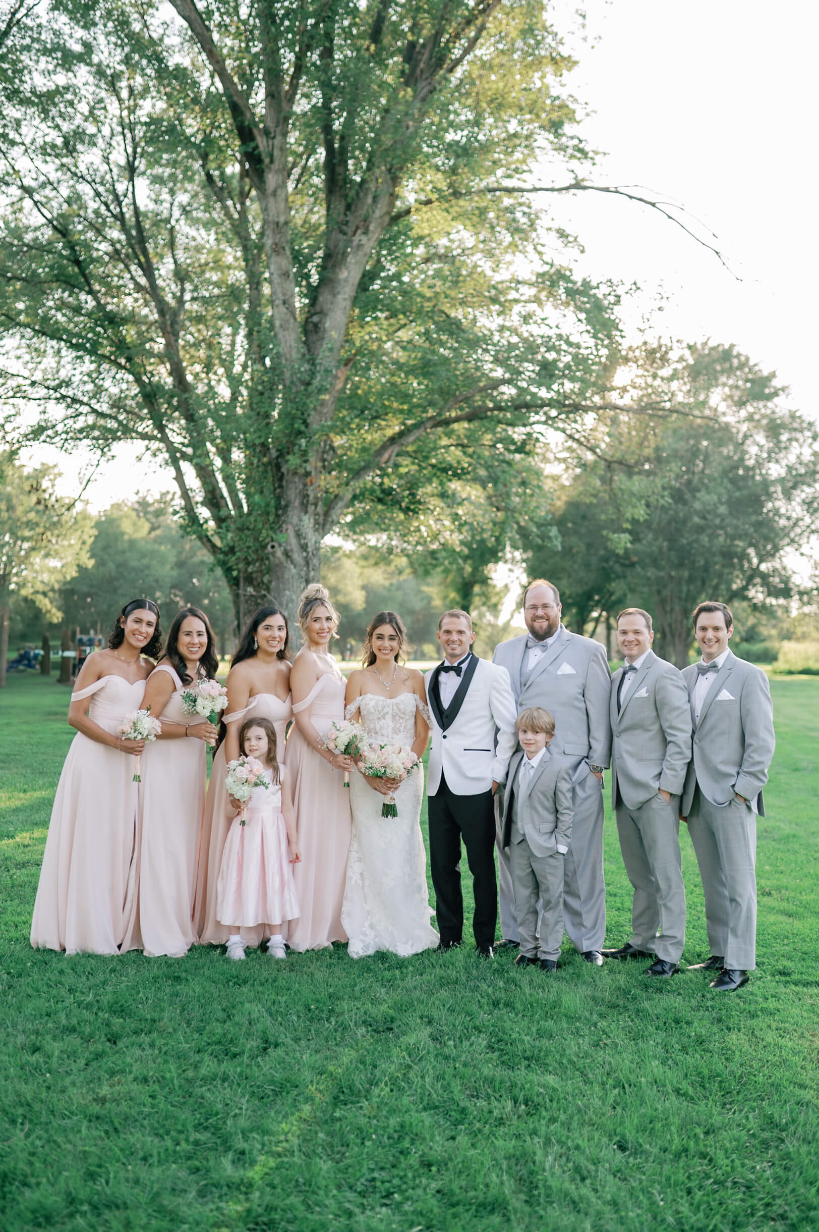 A bride and groom stand with their pink and grey wedding party in a lawn with two young children during their pippin hill farm wedding