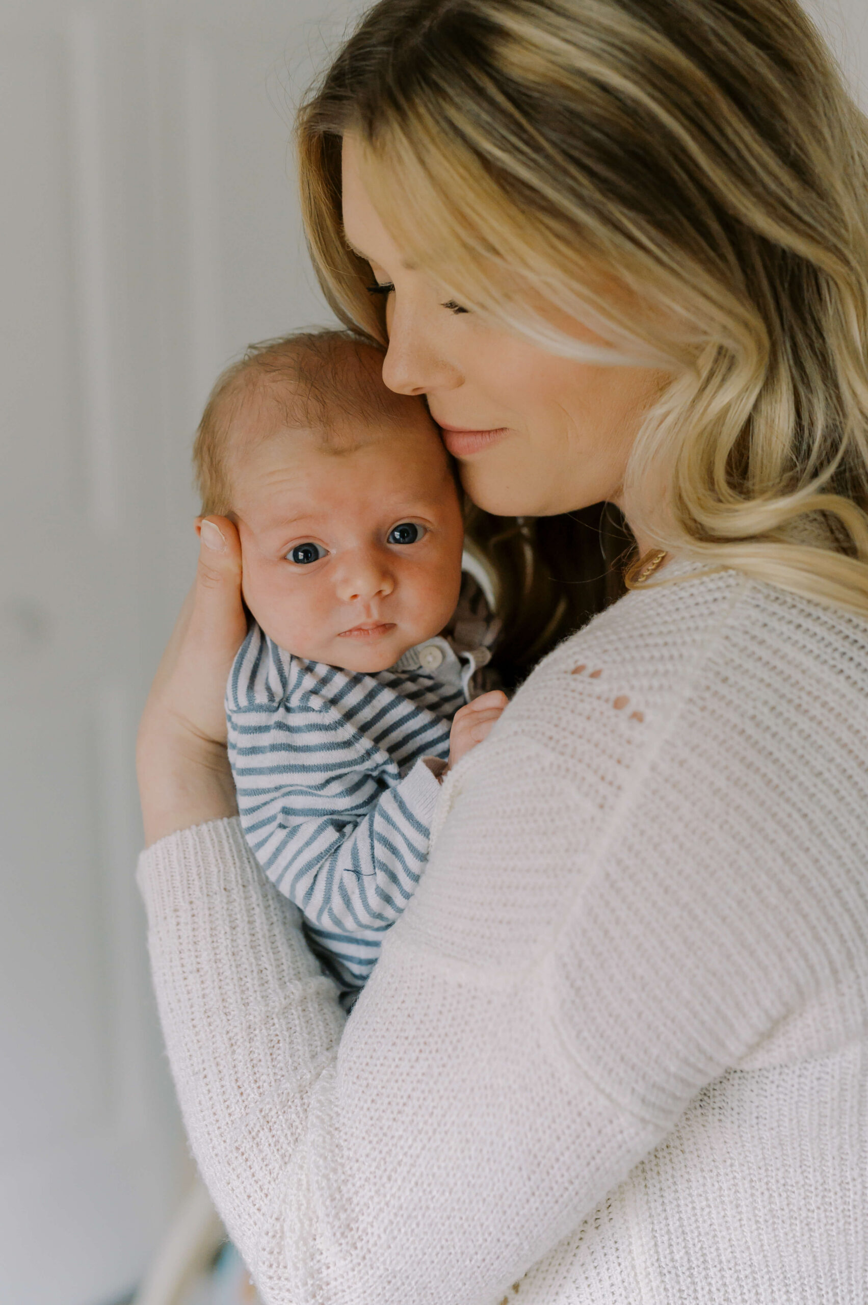 A new mom cradles her newborn against her shoulder with eyes open in blue stripes after meeting nannies in Richmond, VA
