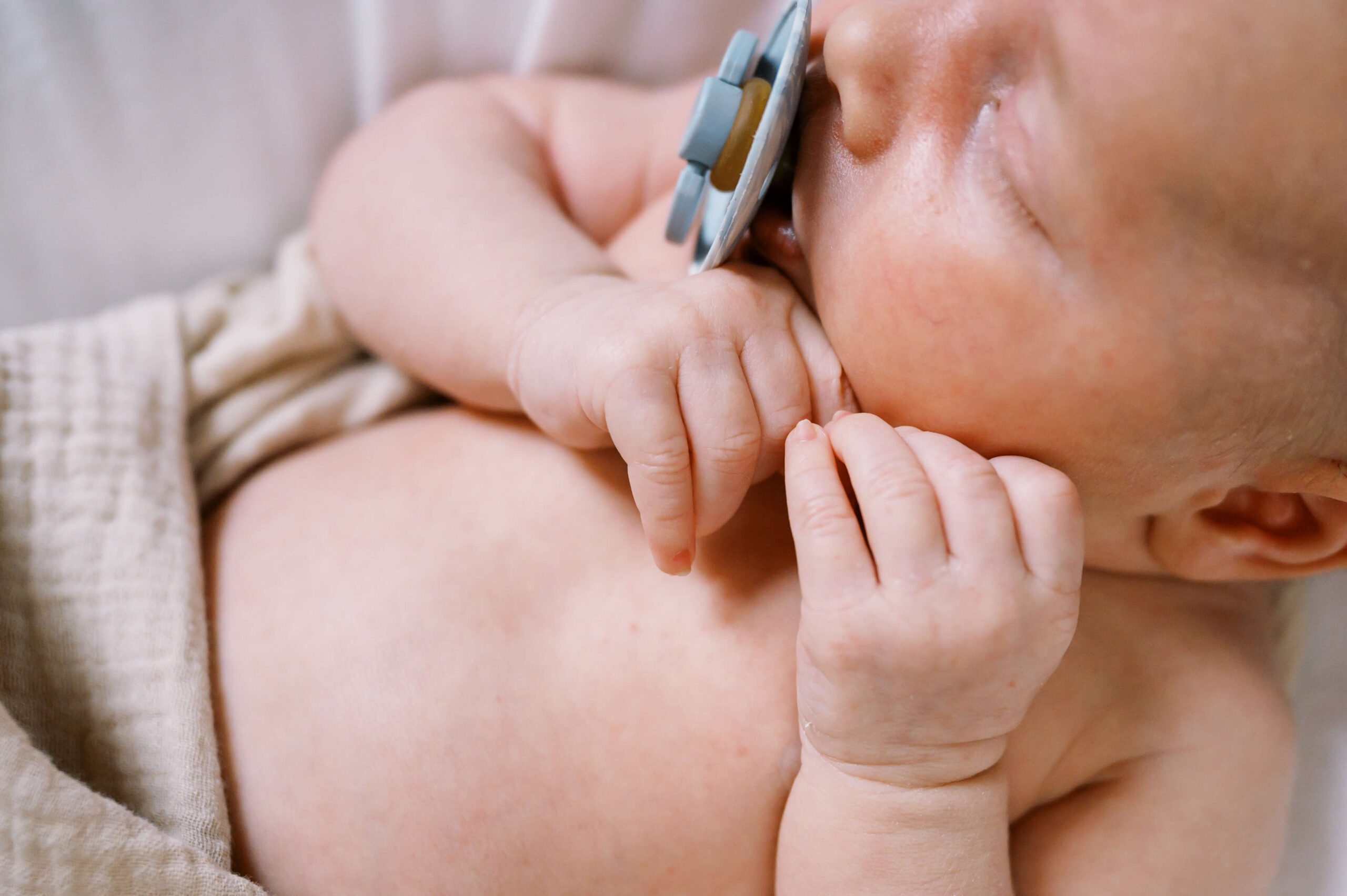 Details of a newborn baby's hands under its chin while sleeping with a pacifier after meeting nannies in Richmond, VA