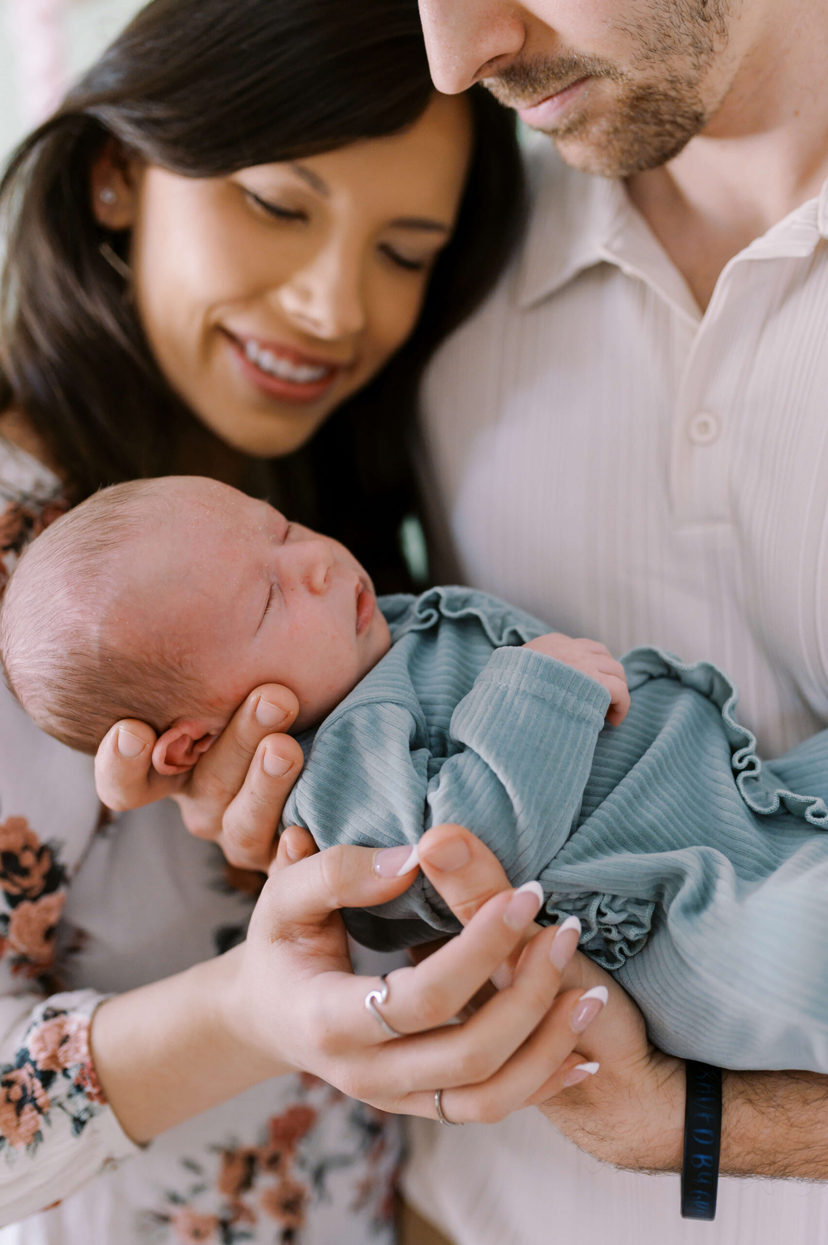 Happy new parents cradle their sleeping newborn baby in a blue onesie thanks to great postpartum doulas in Richmond, VA