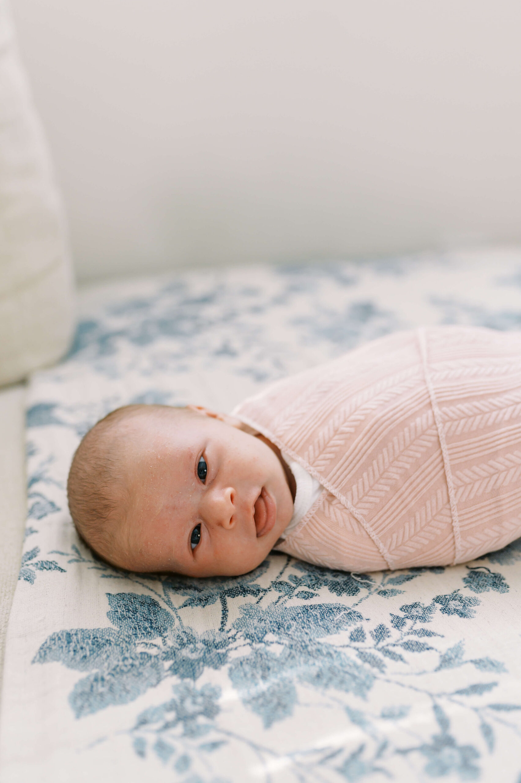 A newborn baby sleeps in a pink swaddle sticking out her tongue on a couch after meeting postpartum doulas in Richmond, VA