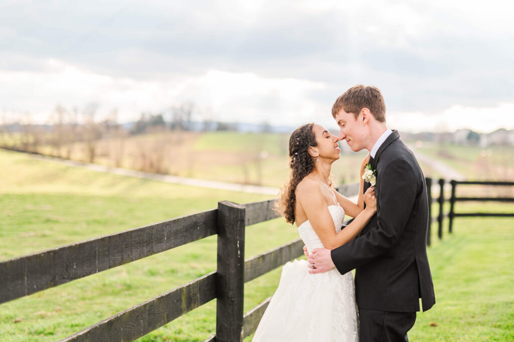 Happy newlyweds lean in for a kiss while standing by a dark wooden fence