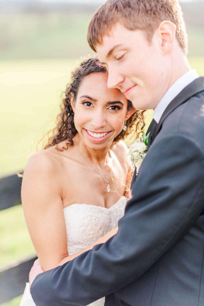 A happy bride smiles while snuggling into her groom in a black tux at sunset during their shadow creek wedding
