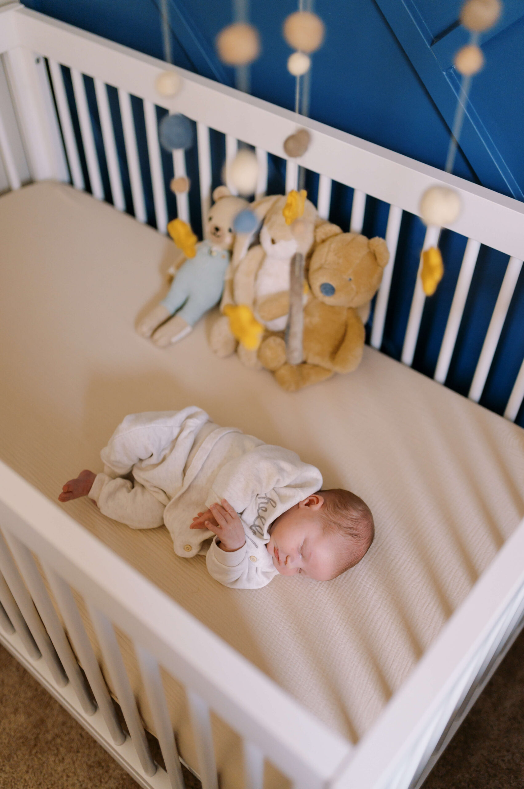 A newborn baby sleeps in a crib with teddies in a white onesie