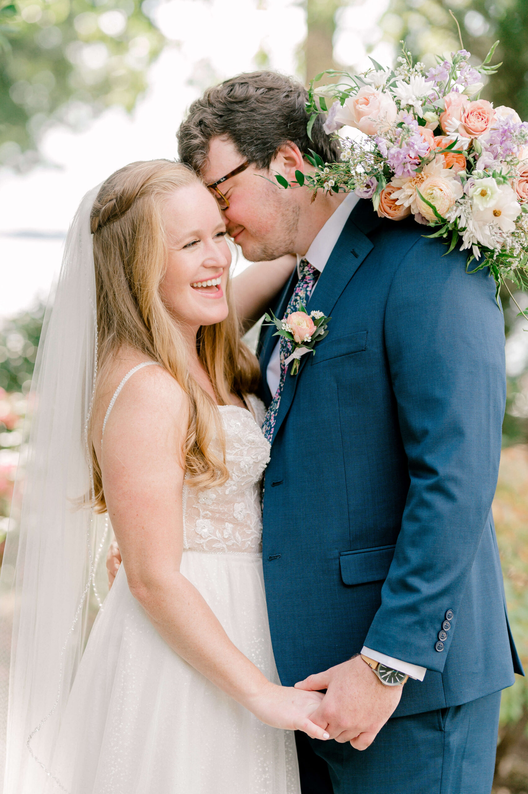A bride laughs while snuggling her groom in blue with her large colorful bouquet behind his head during their the market at grelen wedding