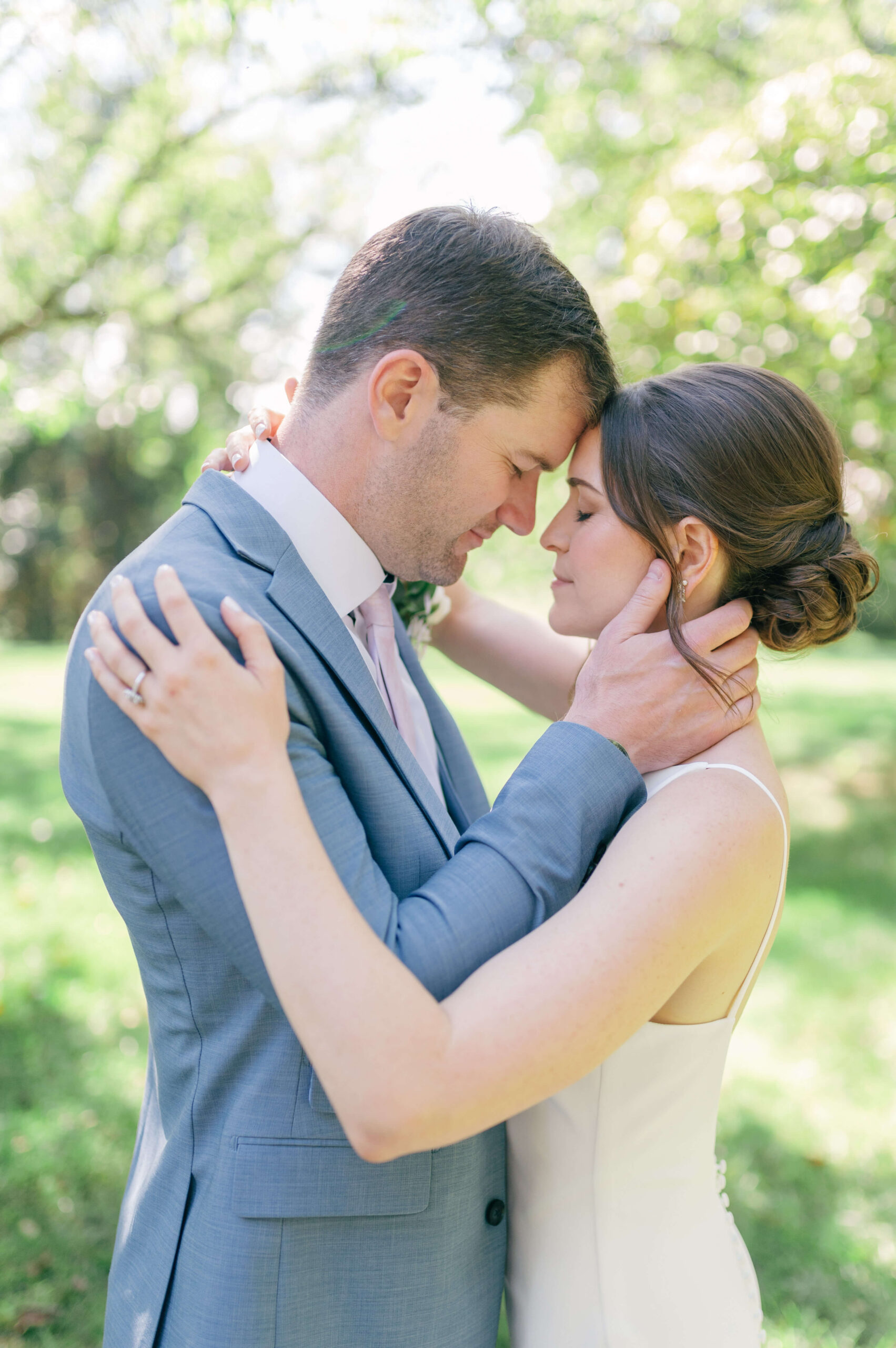A happy newlywed couple touch foreheads and hold each other while standing in a lawn during their veritas winery wedding
